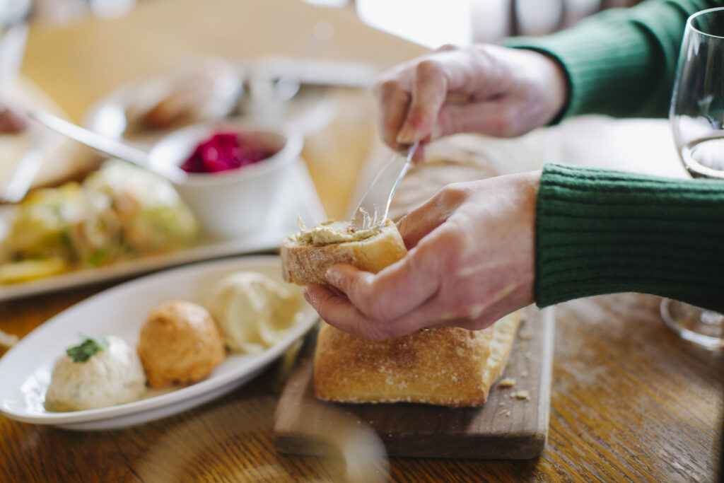 A person spreading cheese on to a baguette.